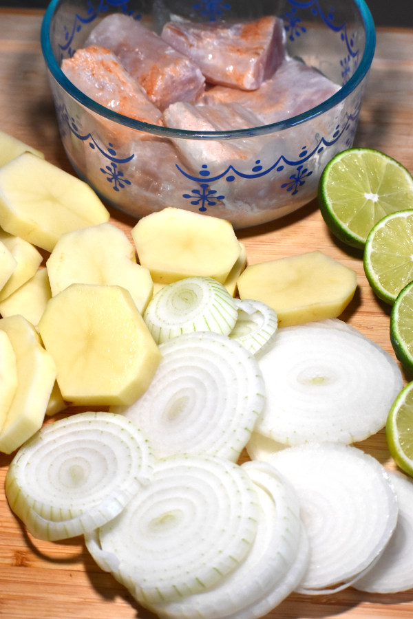 chopped onions, potatoes and limes on a cutting board with marinating fish in the background