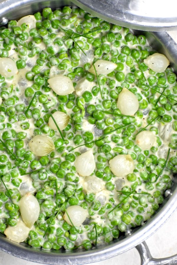 Close up of a pan of creamed peas with pearl onions.