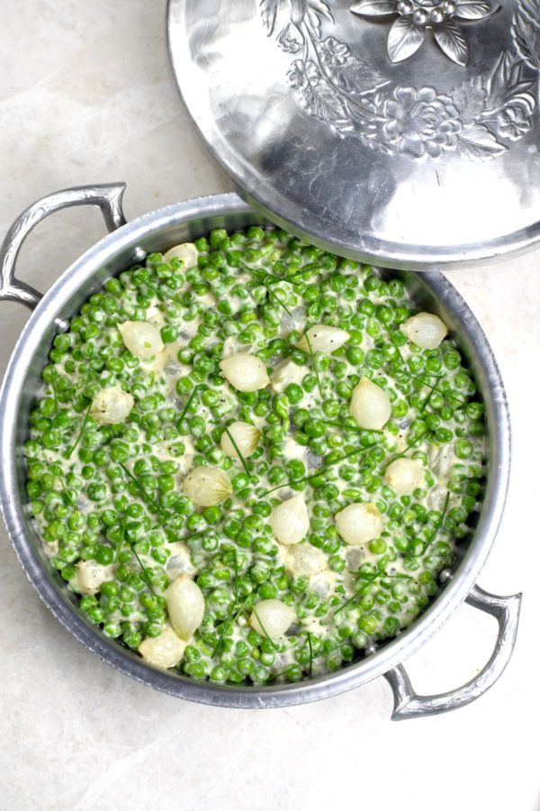 Pan of creamed peas and pearl onions garnished with chives.